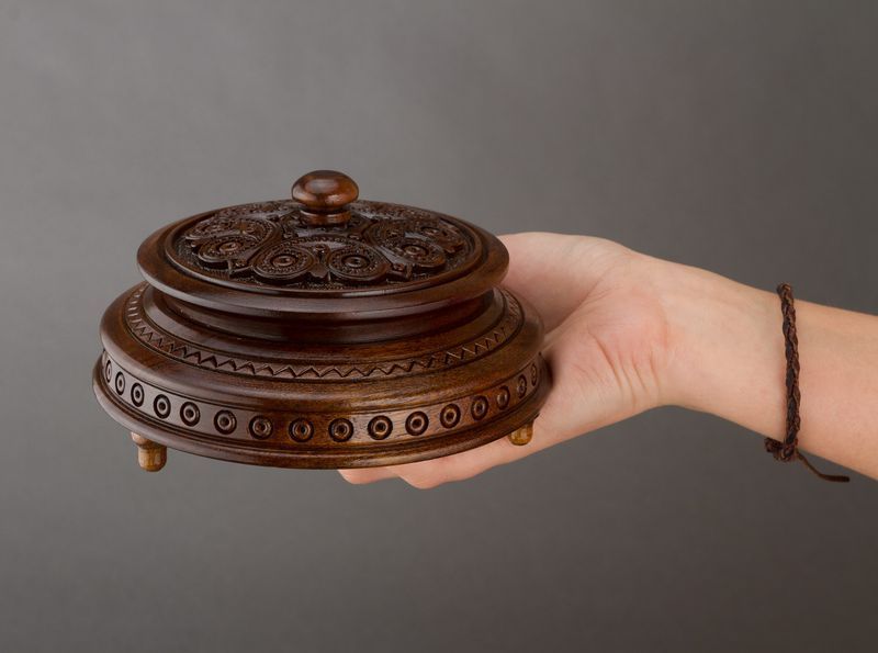 Round figured wooden box with carving and handle.