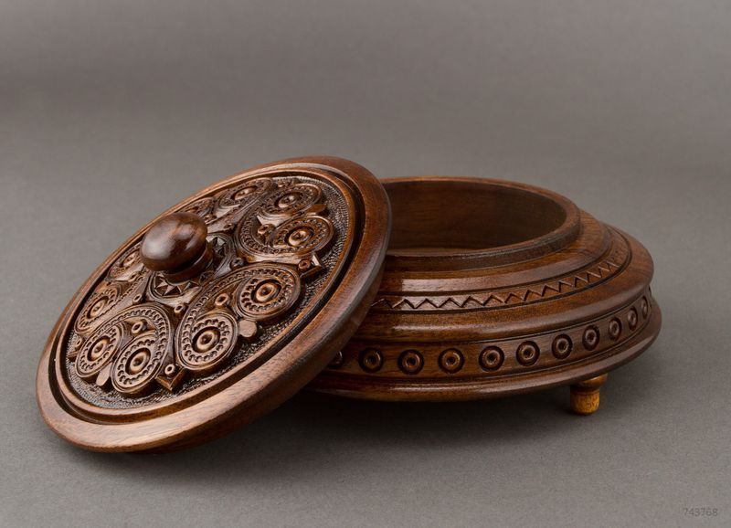 Round figured wooden box with carving and handle.