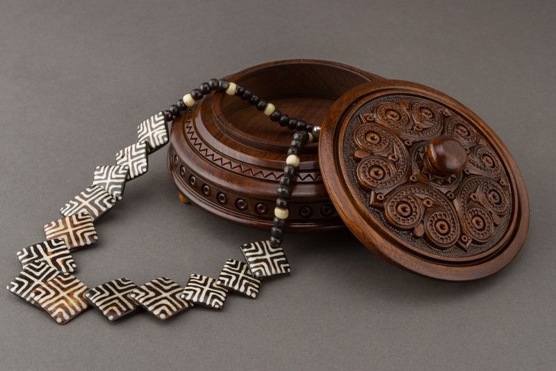 Round figured wooden box with carving and handle.